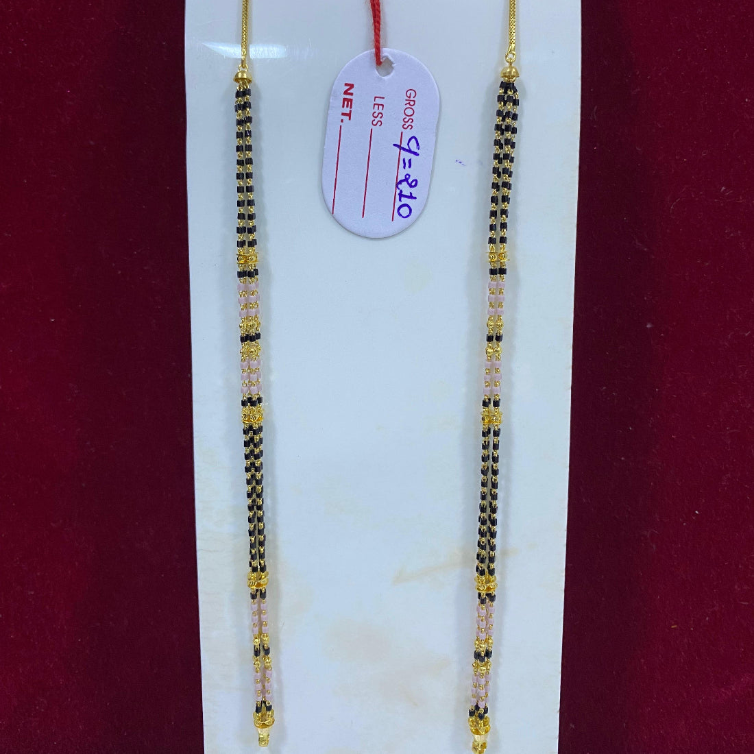 Two gold and black beaded necklaces on a white card with a red background