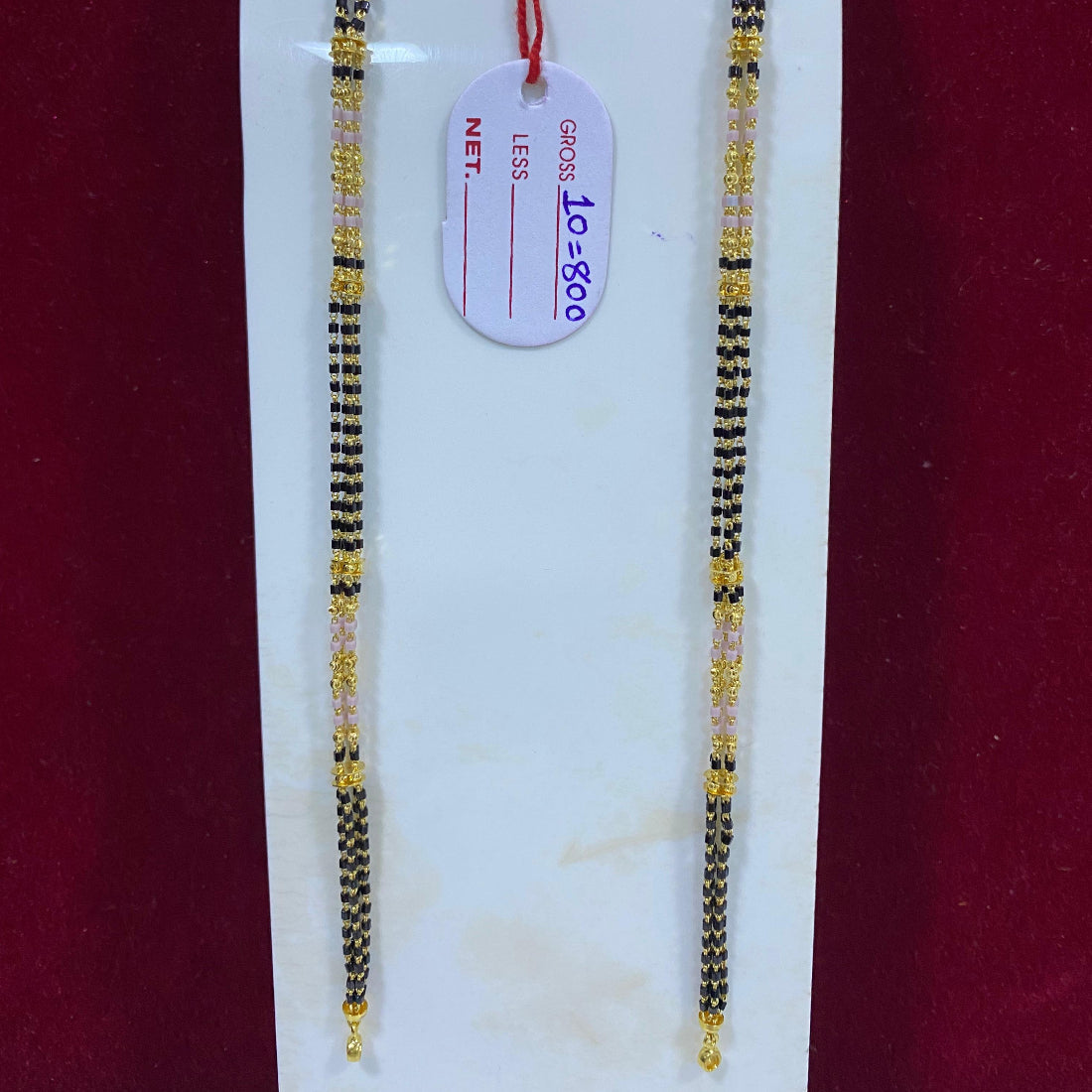 Two gold and black beaded bracelets on a white stand with a red background