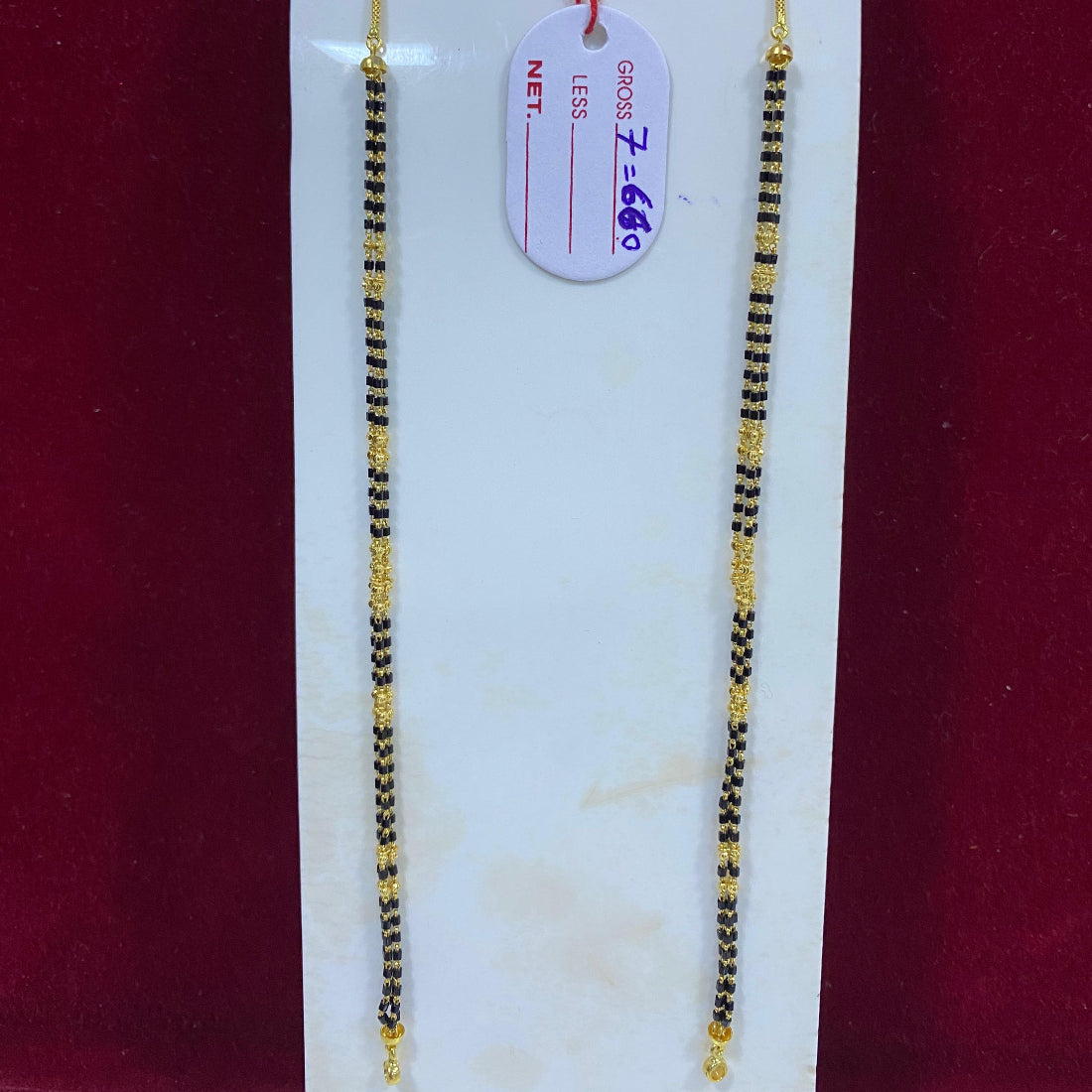 Two gold and black beaded necklaces on a white card with a red background