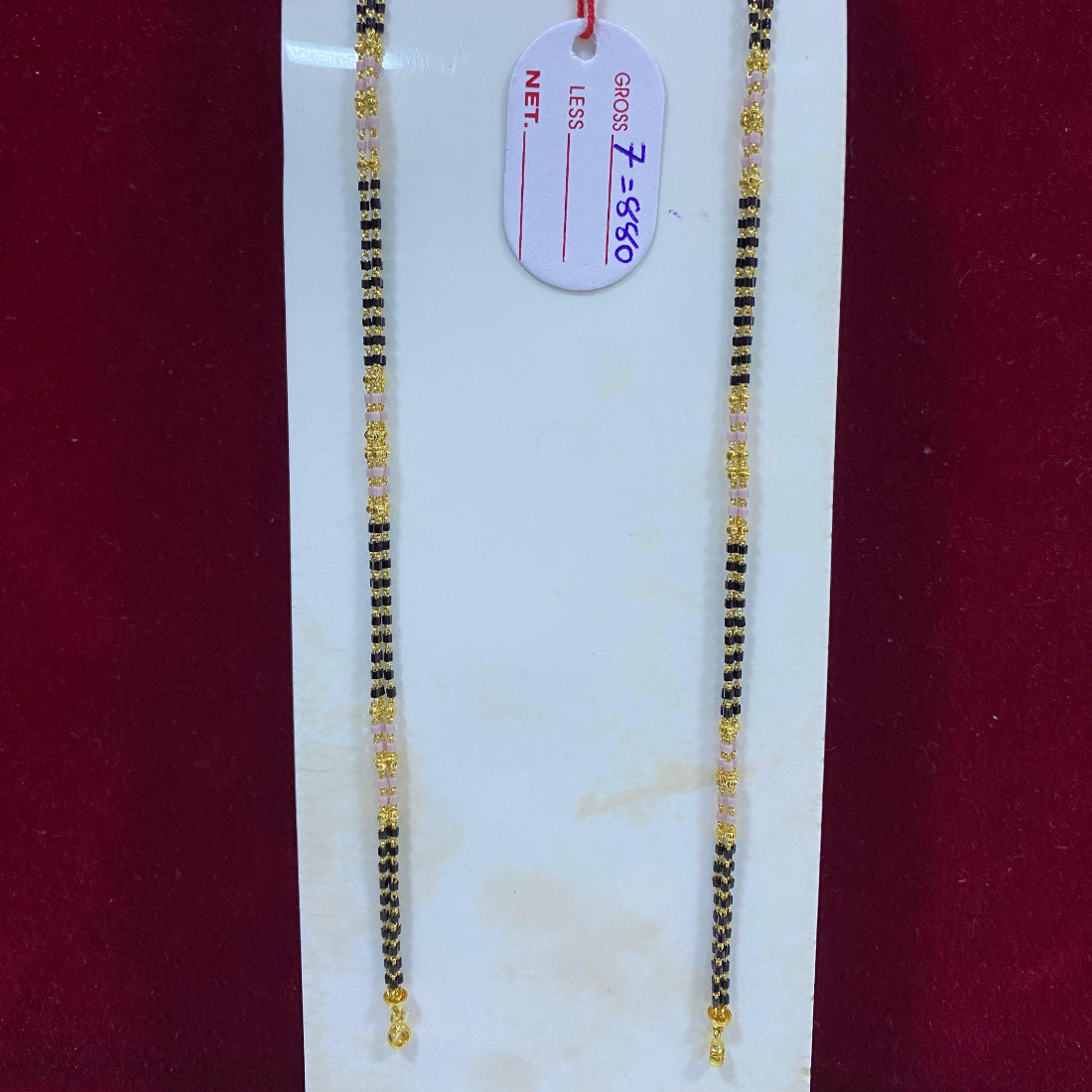 Two gold and black beaded necklaces on a white marble slab with a price tag.