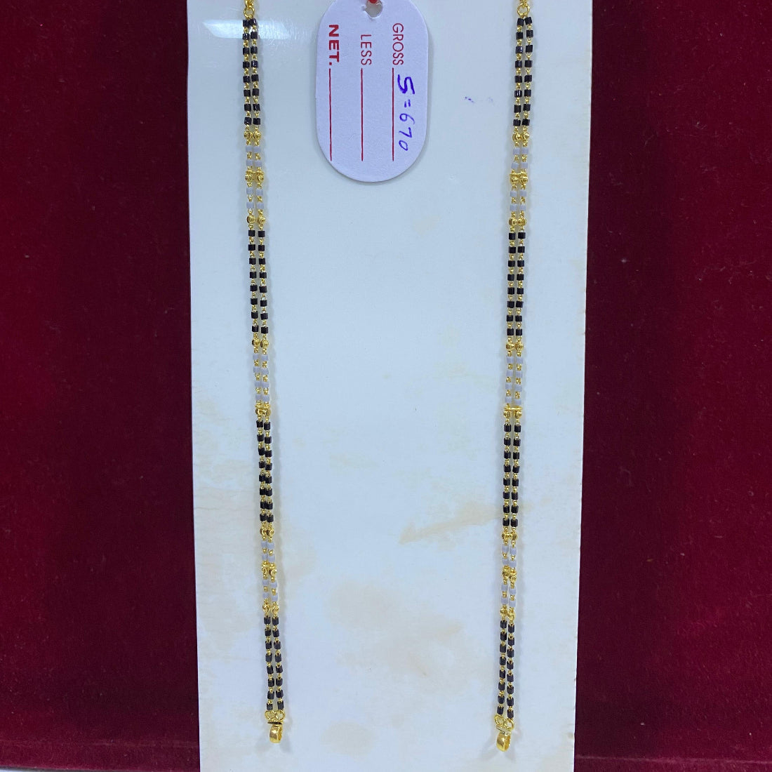 Two gold necklaces on a white card with a red background