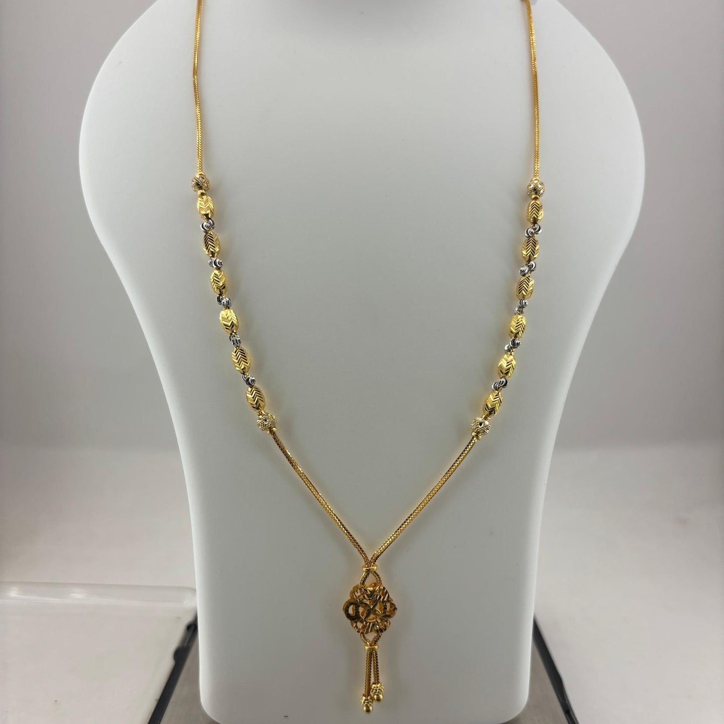 A gold necklace with a key-shaped pendant displayed on a white mannequin bust, with a digital scale visible underneath.