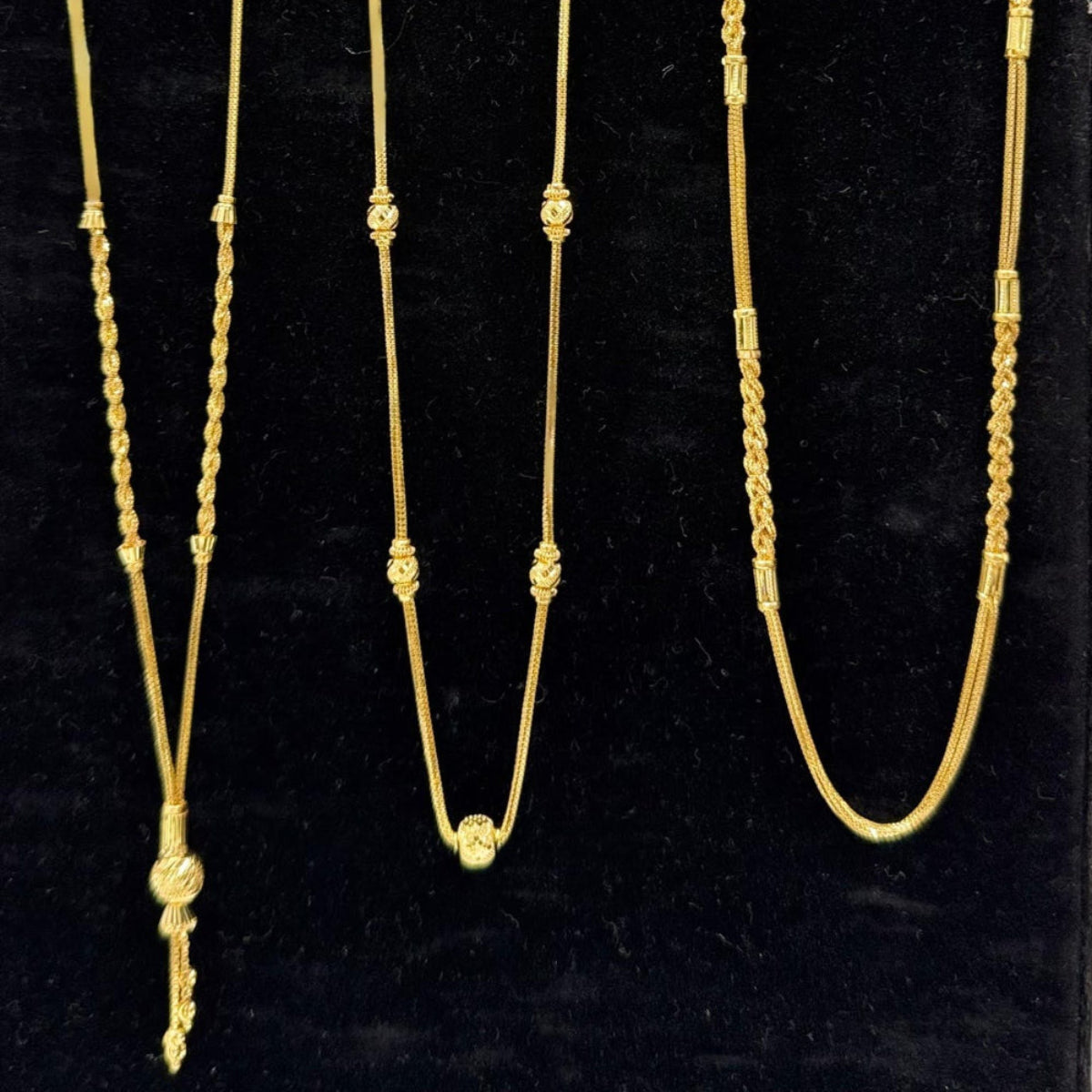 Three gold necklaces on a black velvet stand