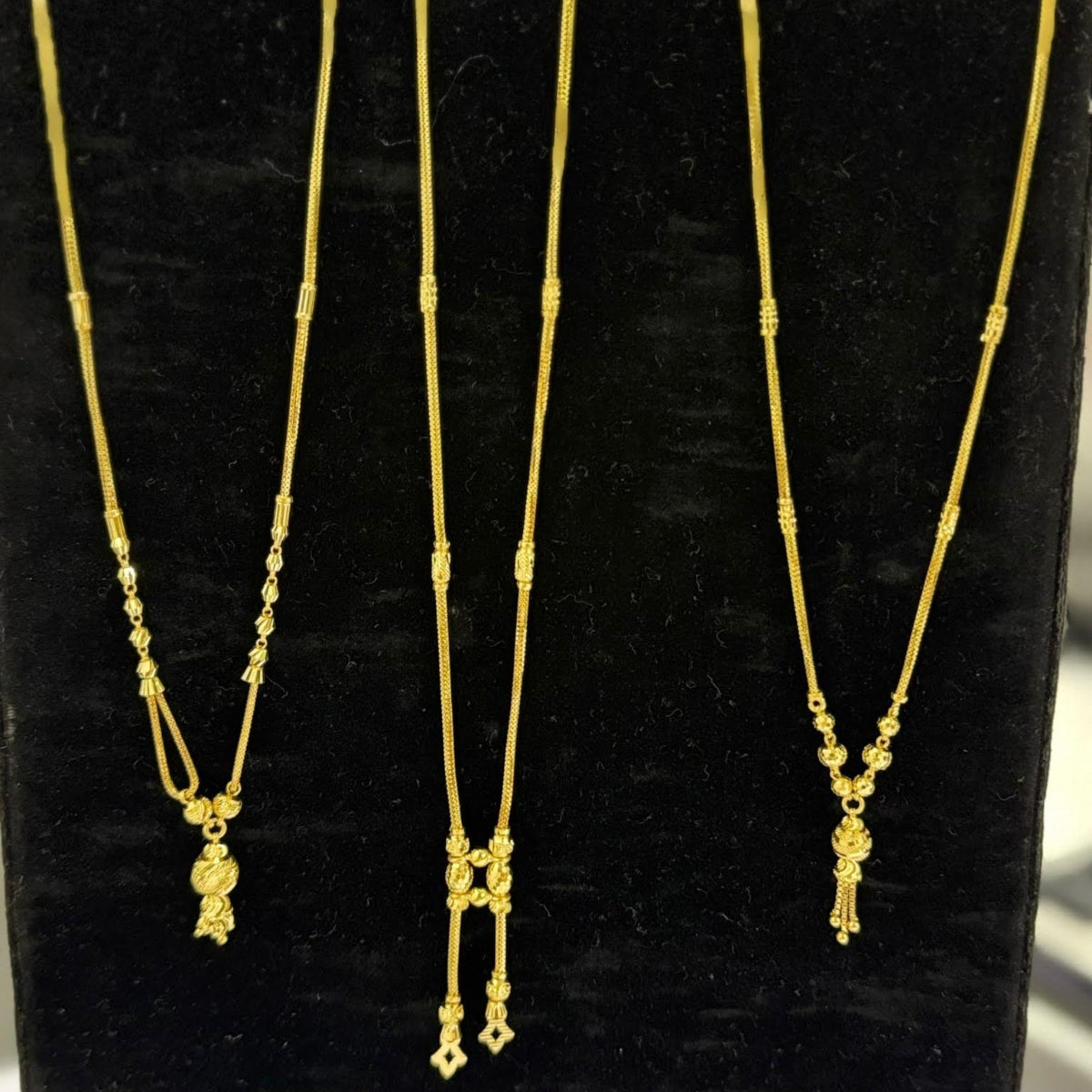Three gold necklaces on a black stand