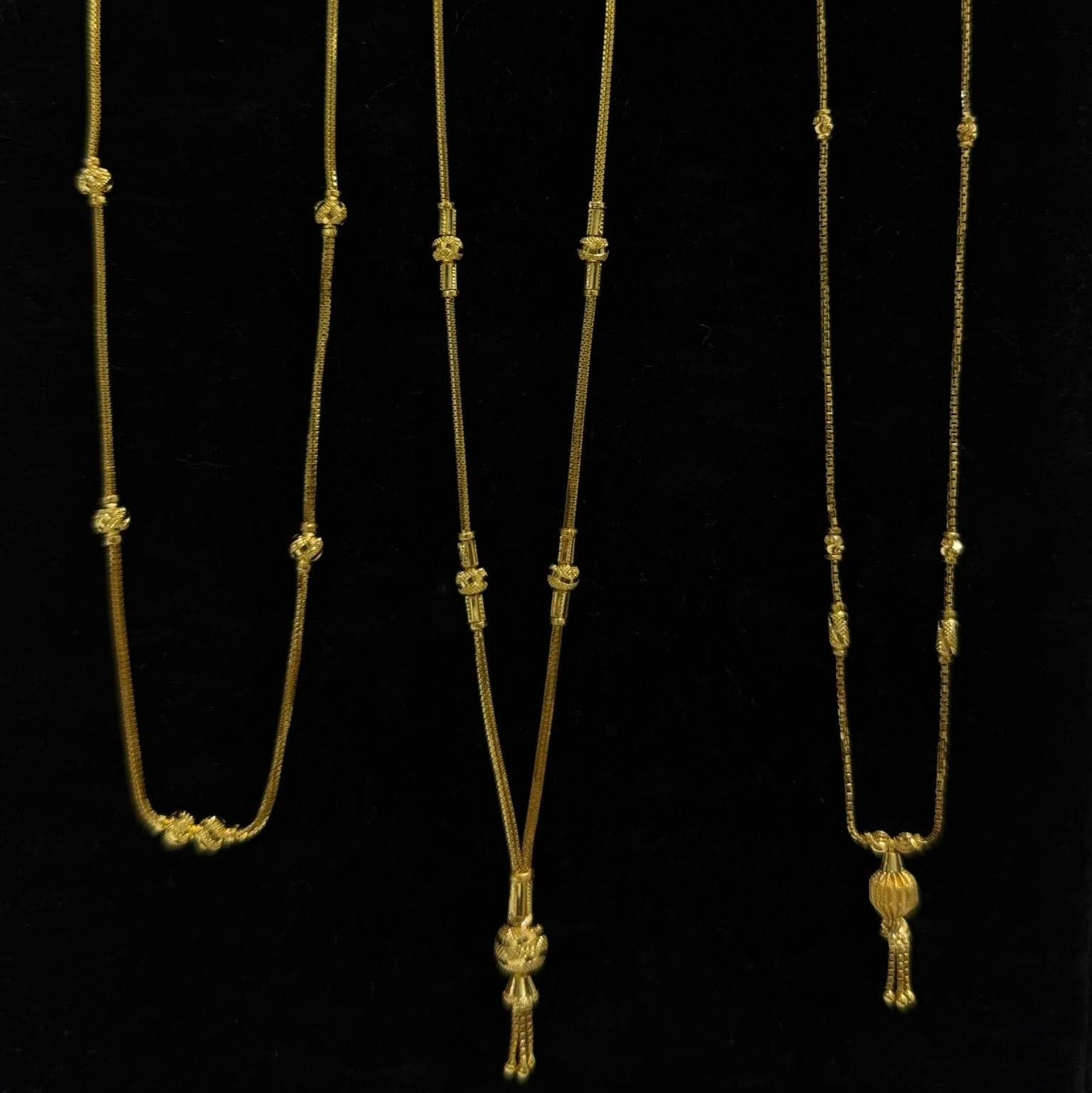 Three gold necklaces on a black stand