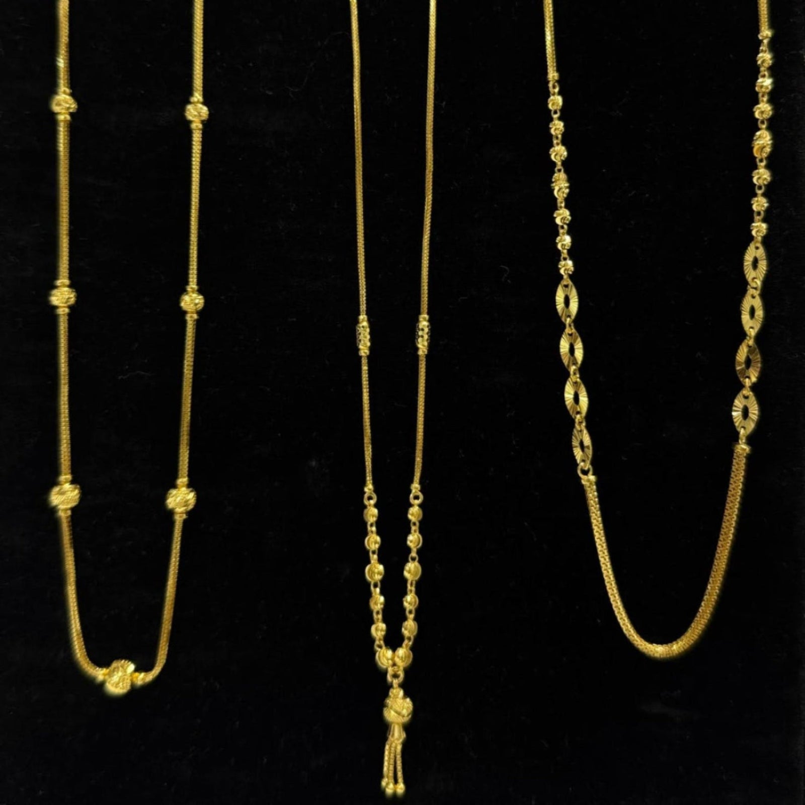 Three gold necklaces on a black stand