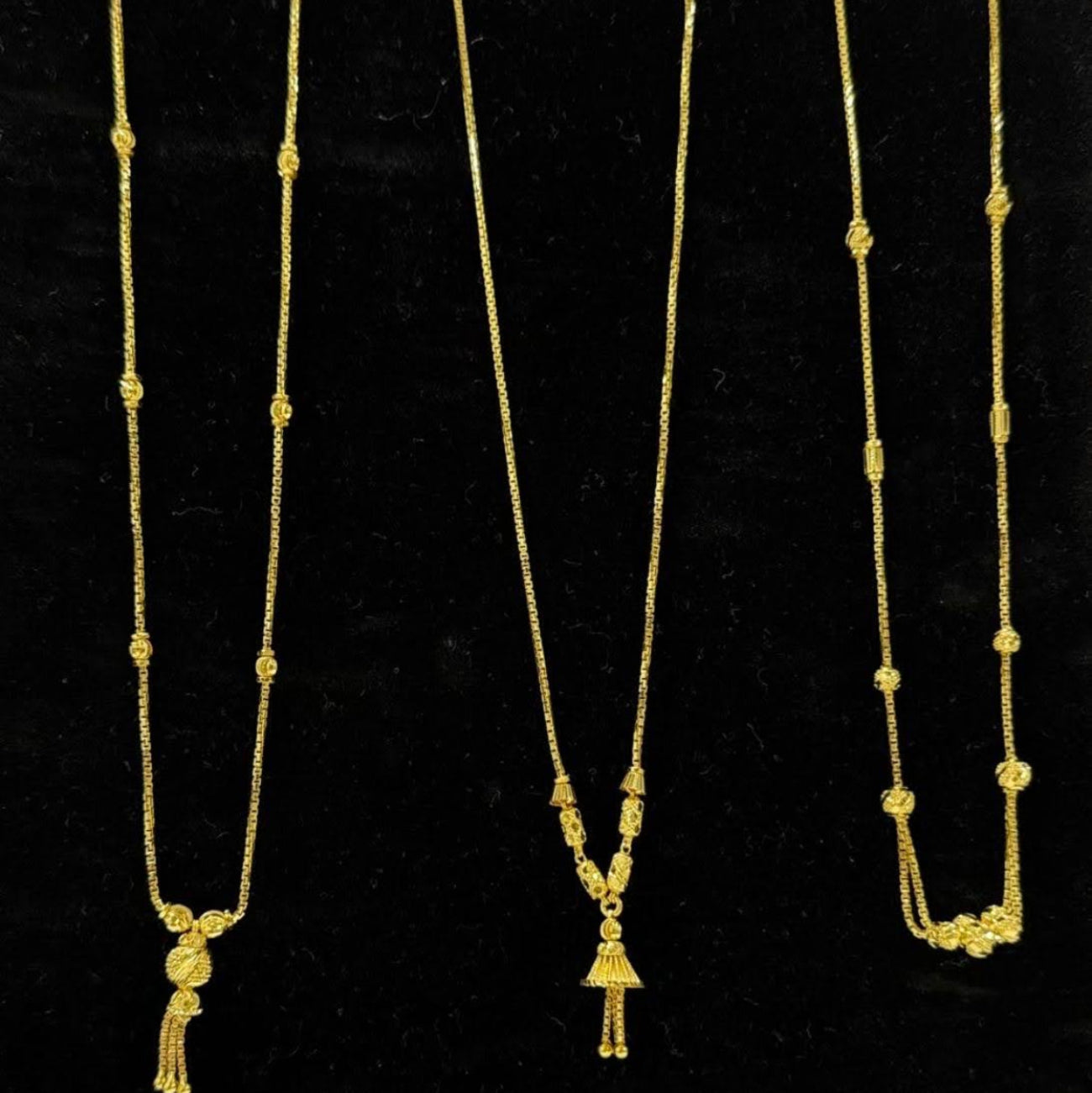Three gold necklaces on a black display stand