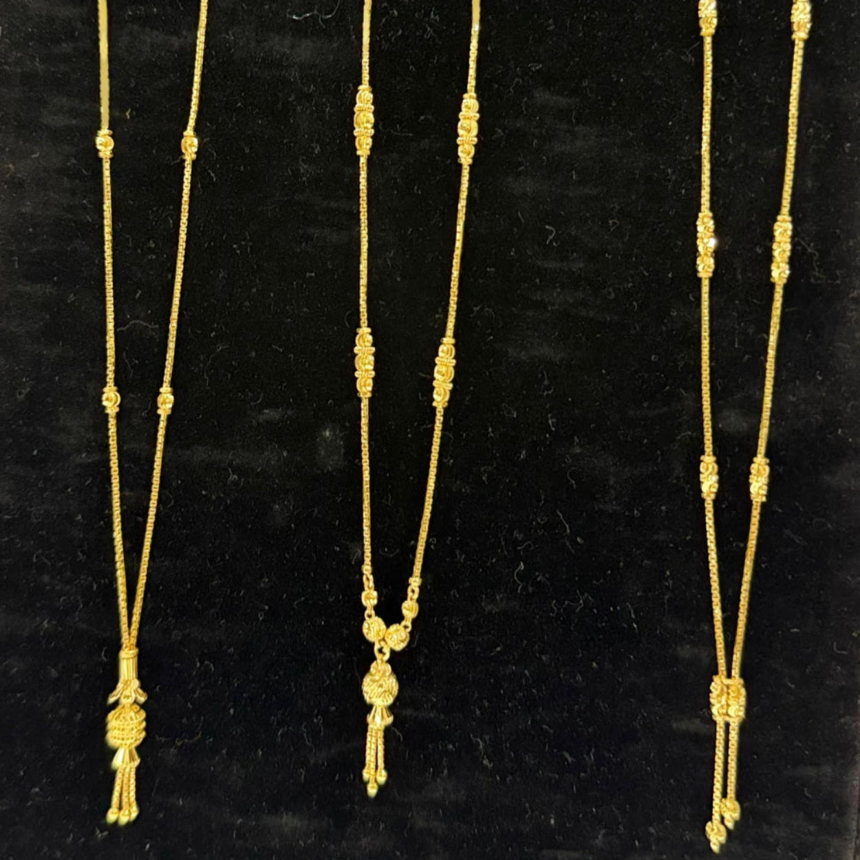 Three gold necklaces on a black stand