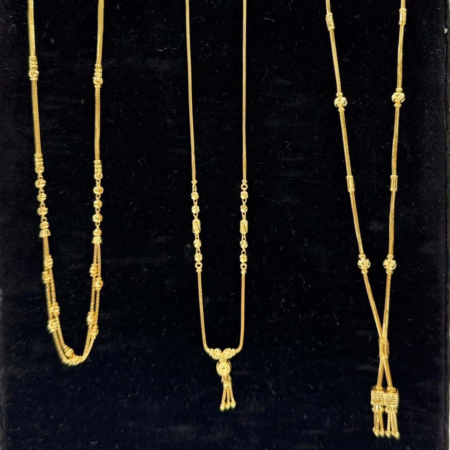 Three gold necklaces on a black stand