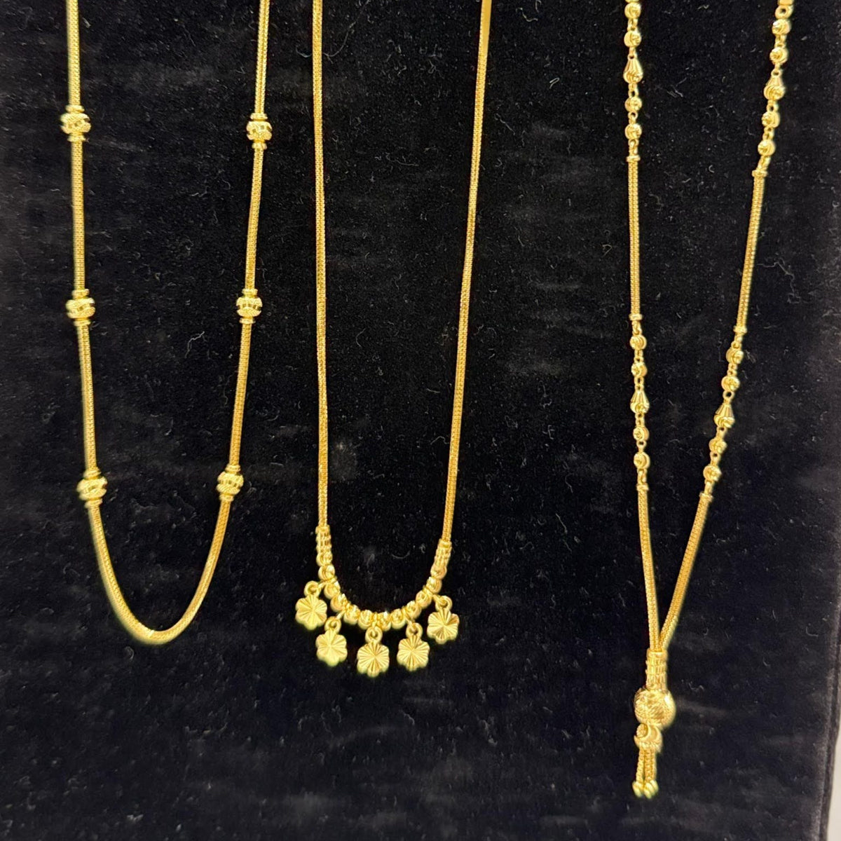 Three gold necklaces on a black stand