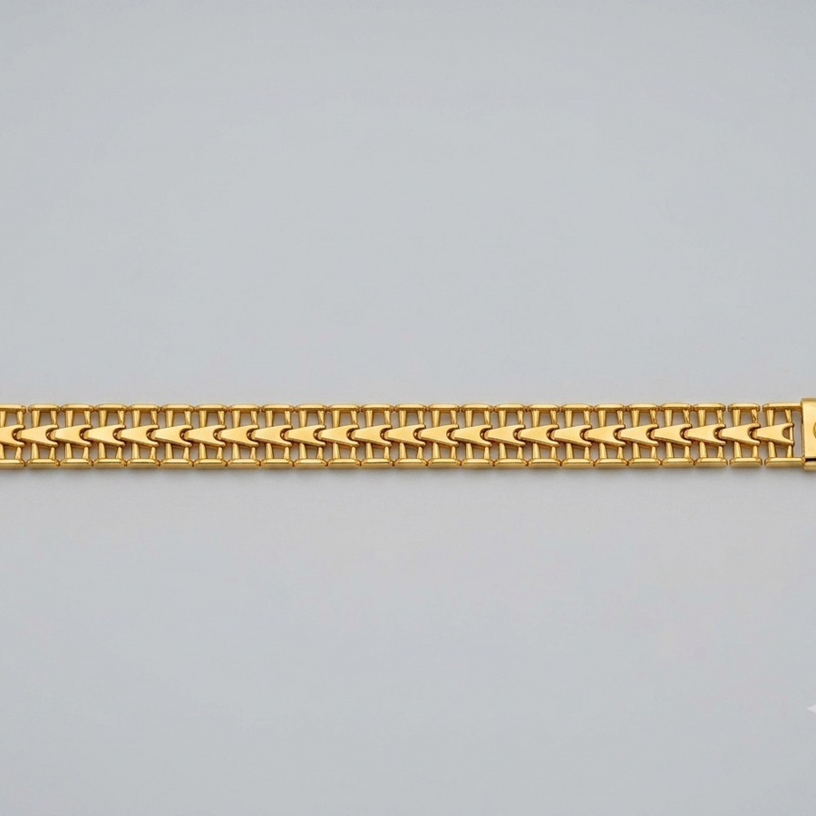 A gold-colored metal link bracelet with a woven chevron pattern, displayed horizontally against a neutral light gray background.