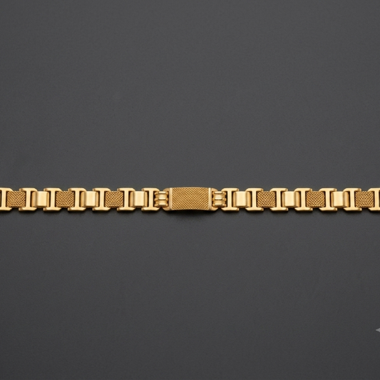 A gold-toned metal link bracelet with a textured center clasp, displayed horizontally on a dark gray background.