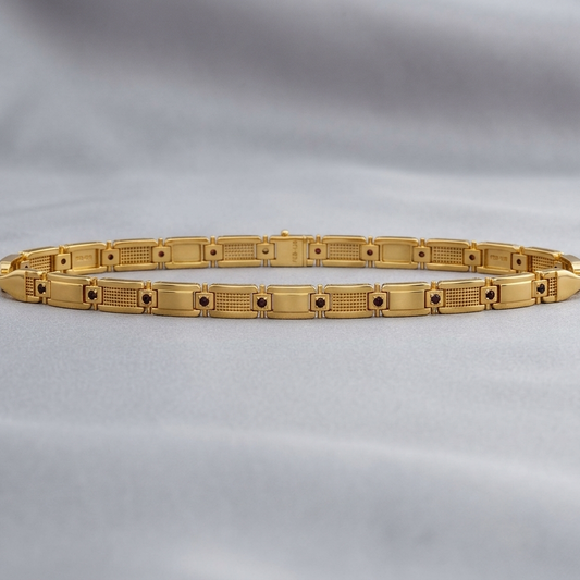 A gold link bracelet with a segmented, geometric design featuring textured and polished rectangular links, displayed on a soft, draped gray fabric background.