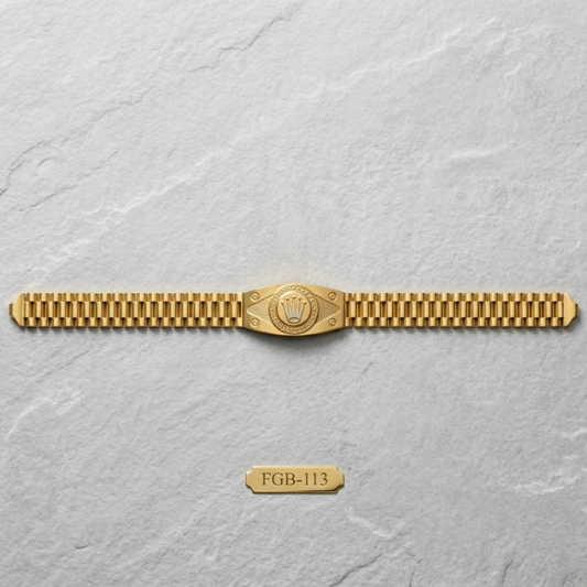 A gold-tone metal watch band with a central shield-shaped emblem, displayed horizontally on a light gray textured background. A small gold tag below reads 'FGB-113'.