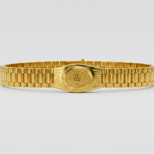 A gold-tone metal link bracelet watch band with a central oval plate featuring a crown emblem, photographed against a clean light gray background.