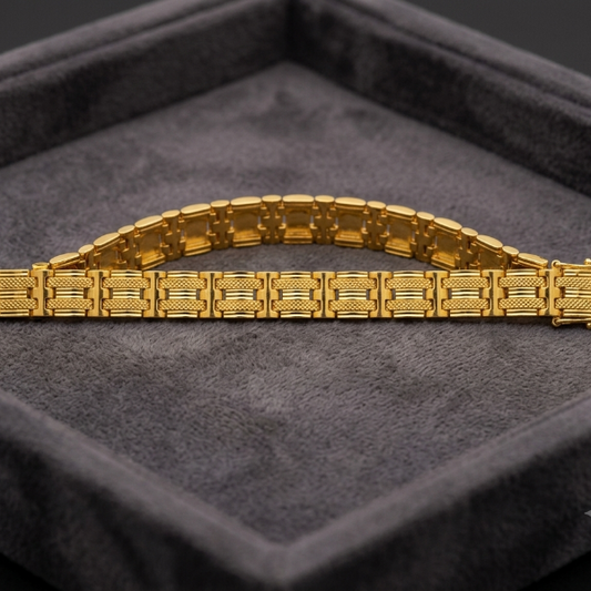 A gold bracelet with a textured, geometric link design, displayed on a dark gray velvet jewelry box.