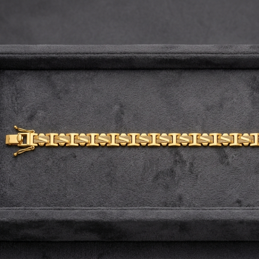 A gold link bracelet with a distinctive bow-shaped clasp, displayed horizontally on a dark gray velvet jewelry box.