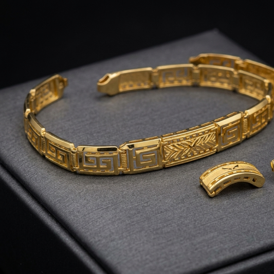 A gold bracelet with geometric cutout patterns, shown open with its clasp removed, resting on a dark gray textured jewelry box against a black background.