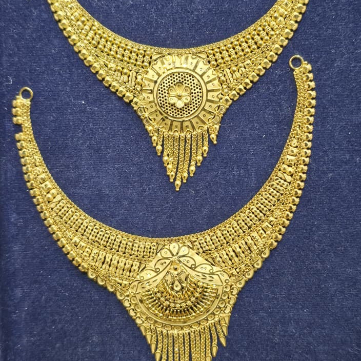 A pair of ornate gold-toned traditional necklace sets displayed on a dark blue velvet surface. The top necklace is a wide curved collar-style necklace with a circular central motif and dangling fringe.