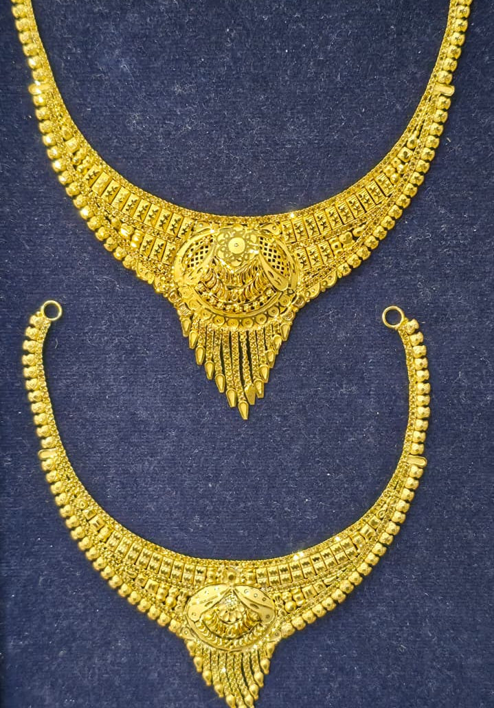 A pair of traditional Indian gold-plated necklace sets, featuring a larger choker-style necklace and a matching choker necklace with a curved collar design, displayed on a dark blue velvet background.