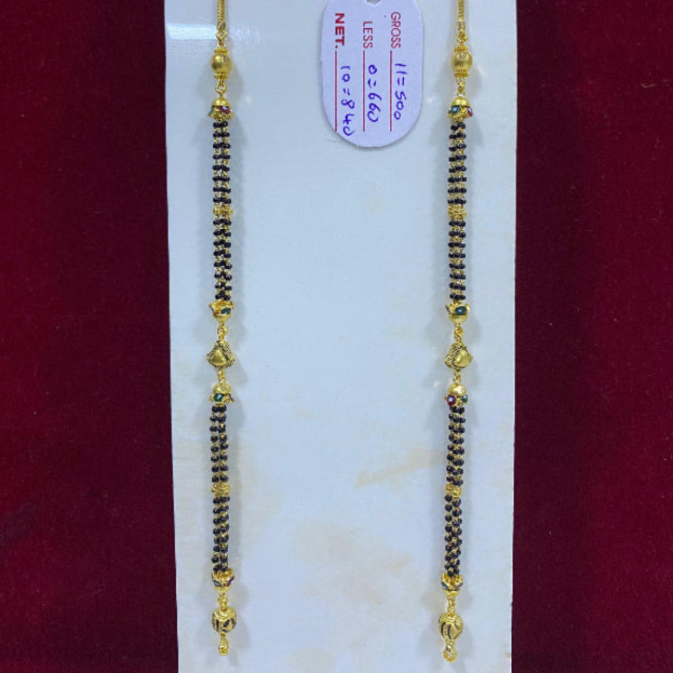 Two gold and black beaded necklaces on a white card with a red background