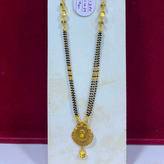 A gold and black beaded necklace with a round gold pendant, displayed on a white jewelry stand against a dark red background.