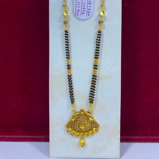 A traditional Indian gold and black bead necklace with a detailed gold pendant, displayed on a white stand against a dark red background.