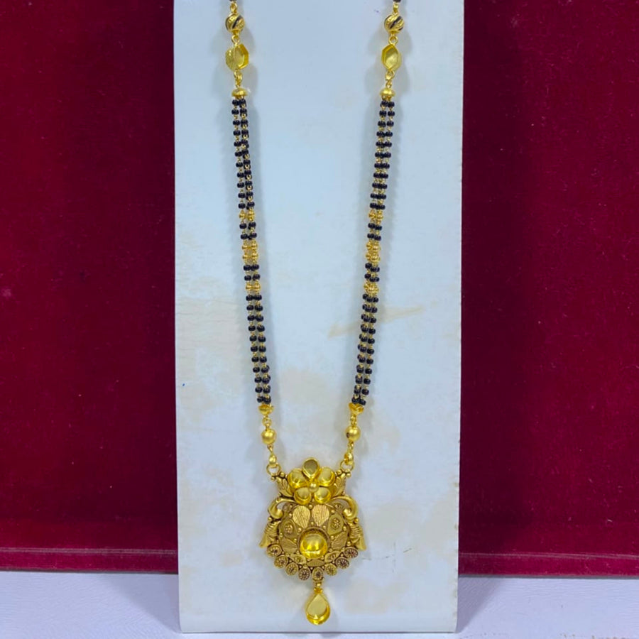 A traditional Indian gold-plated necklace with a black bead chain and an ornate gold pendant, displayed on a white stand against a dark red background.