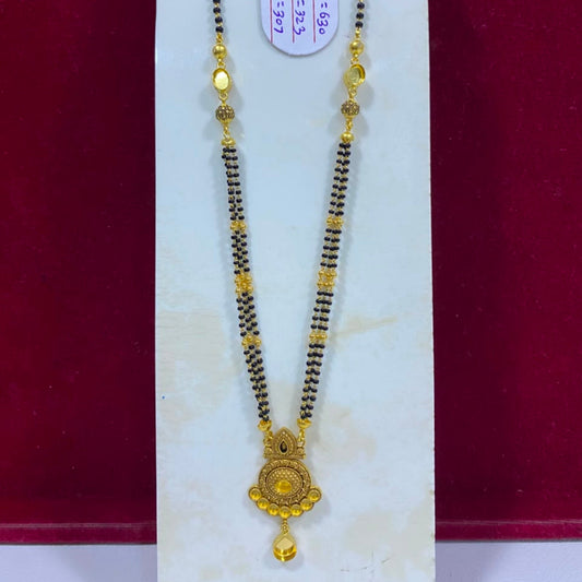 A traditional Indian gold and black beaded necklace (Magga) with a detailed gold pendant, displayed on a white jewelry stand against a dark red background.