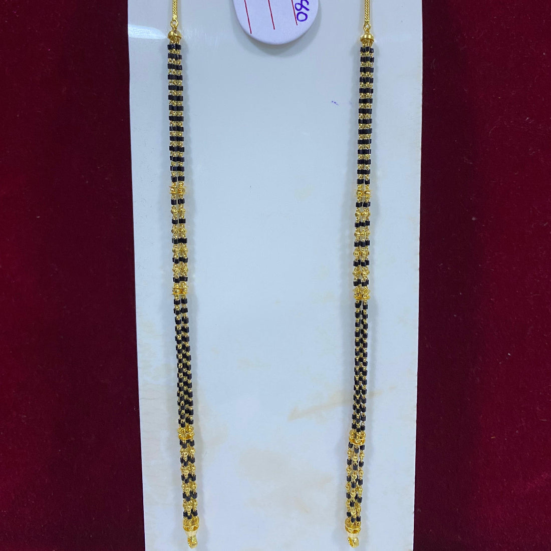 Two gold and black beaded hair strands on a white card with a red background