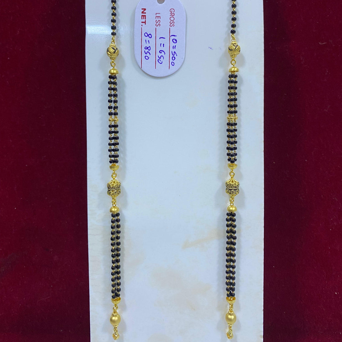 Two gold and black beaded necklaces on a white stand with a red background
