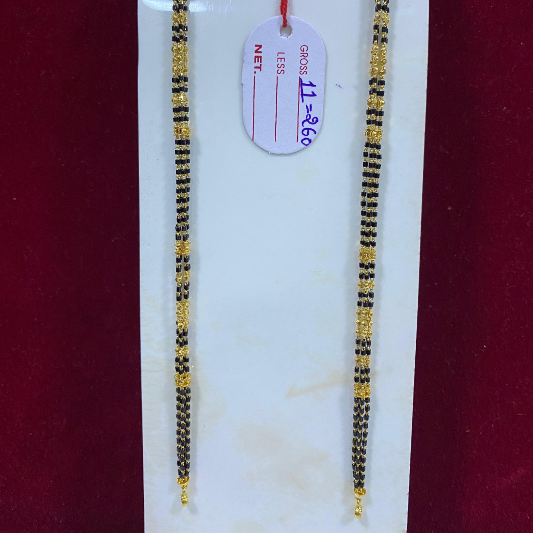 Two gold and black beaded necklaces on a white card with a red background
