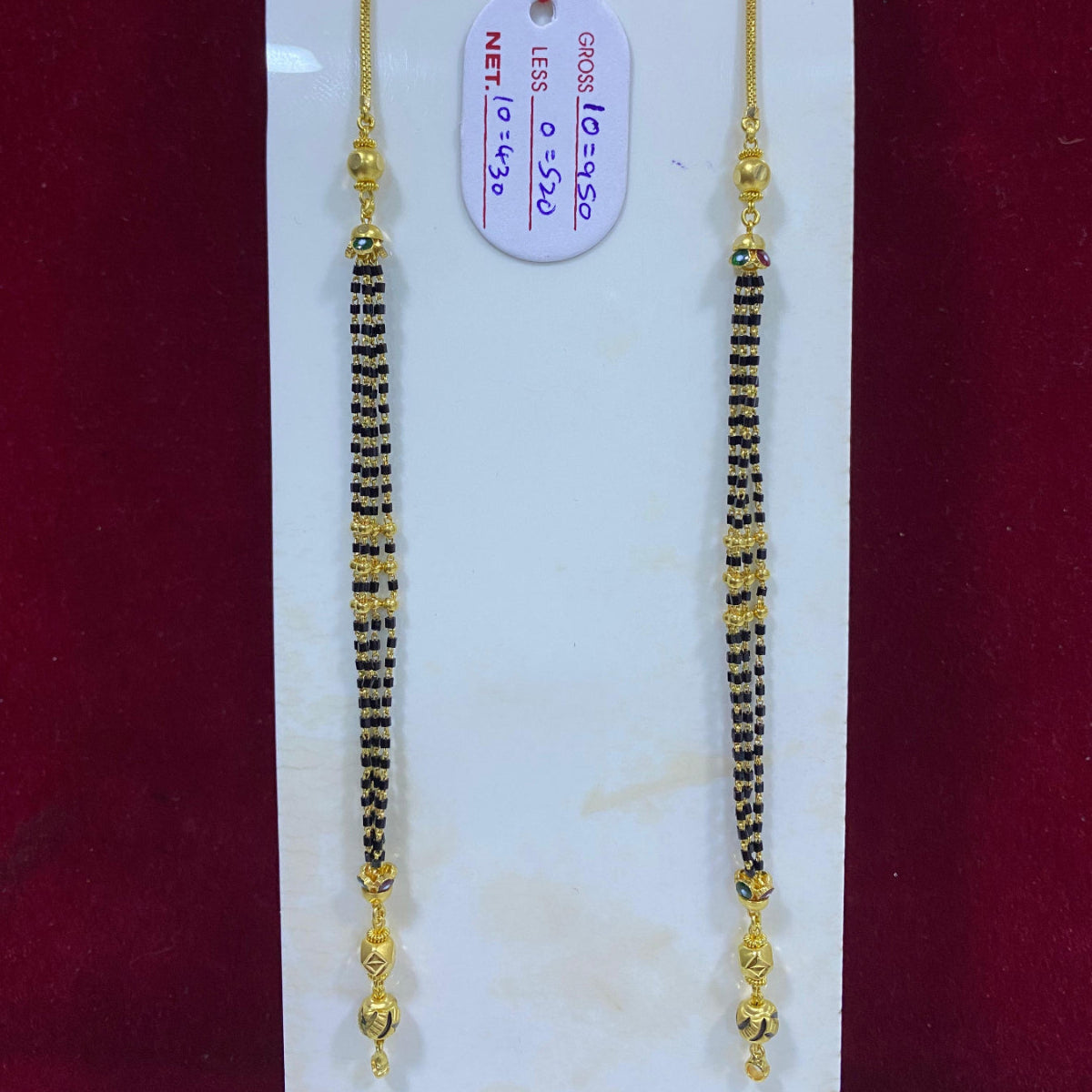 Two gold and black beaded necklaces on a white card with a red background