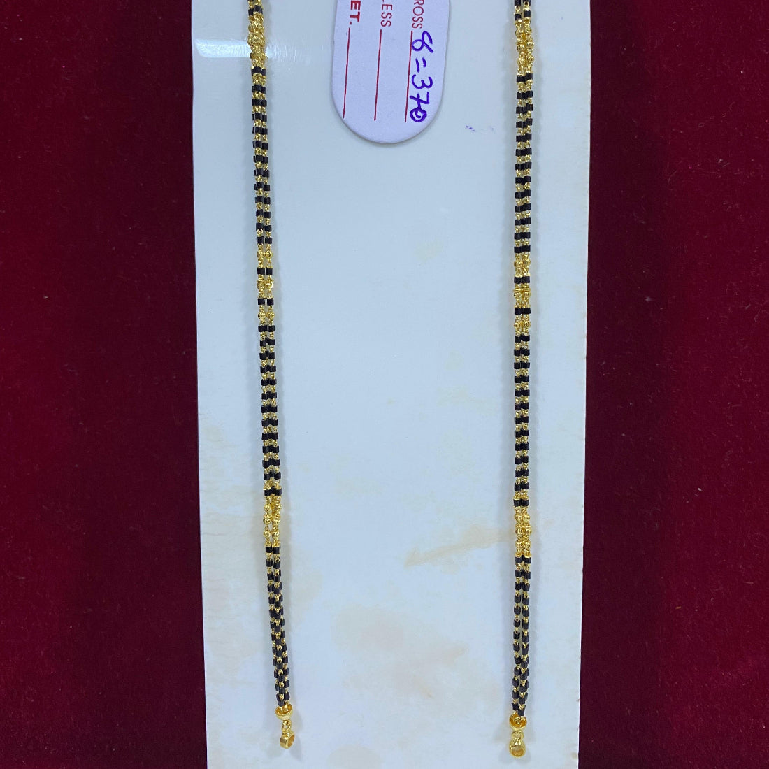 Two gold necklaces on a white stand with a red background