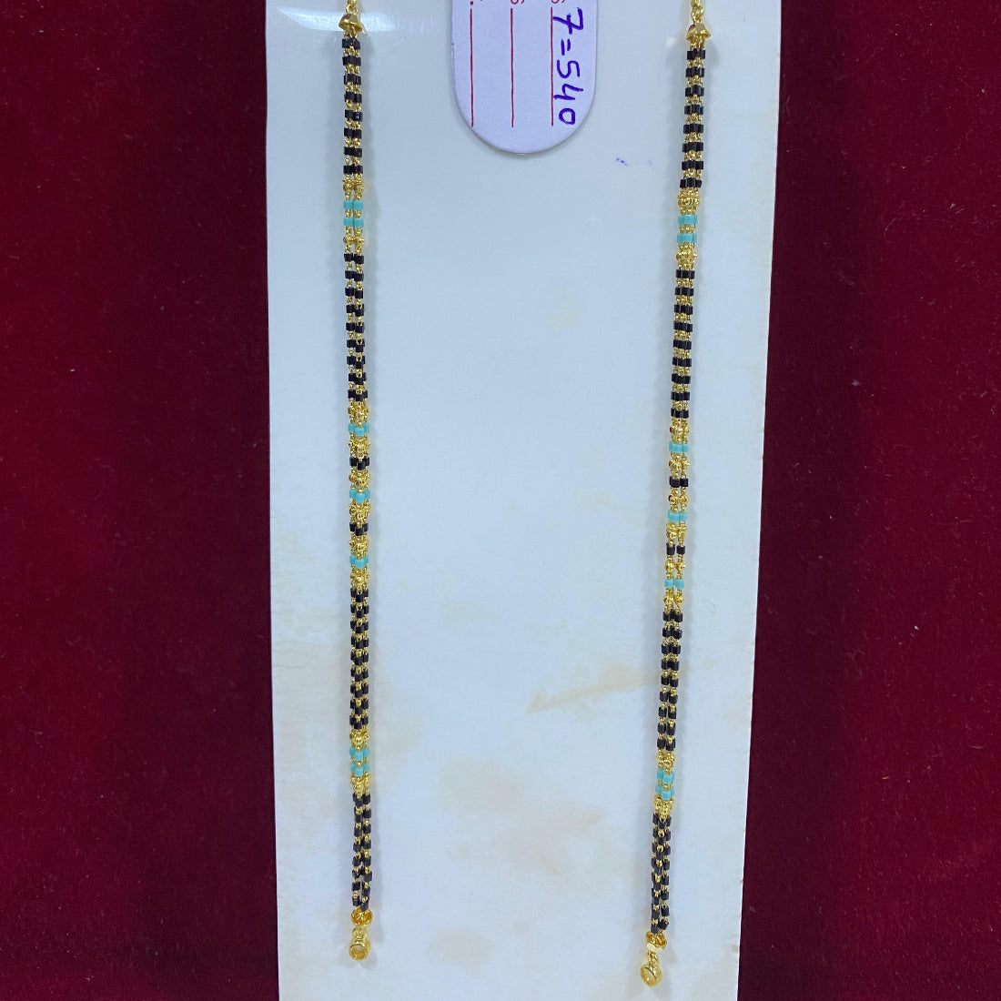 Two beaded necklaces on a white card with a visible tag, against a red background.