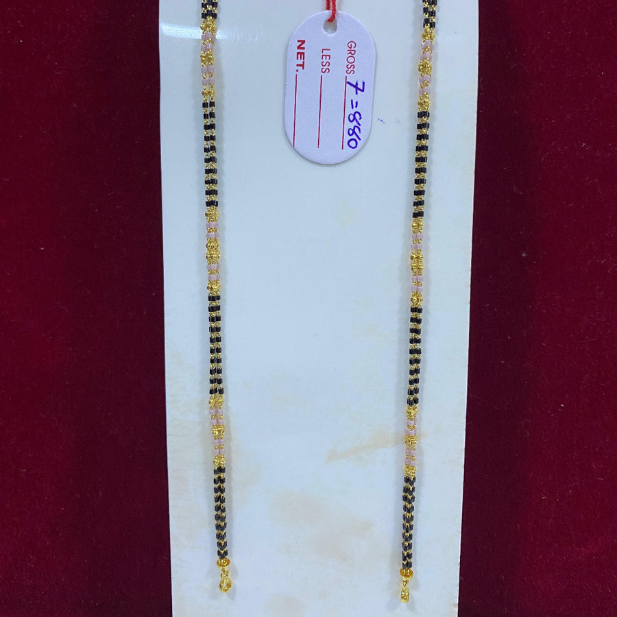 Two gold and black beaded necklaces on a white marble slab with a price tag.