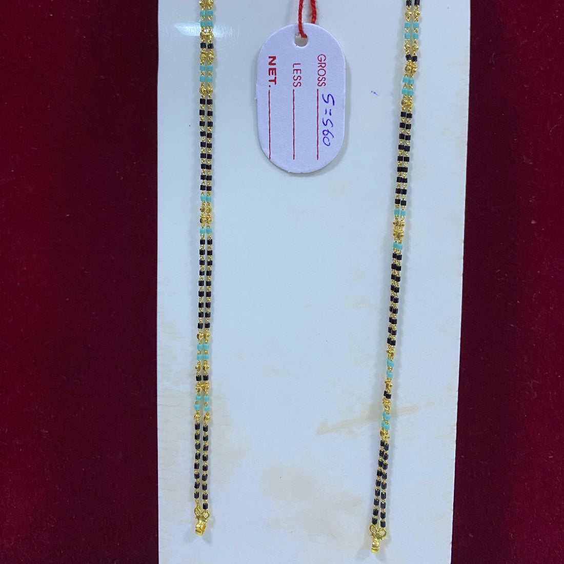 Two gold necklaces on a white card with a red background