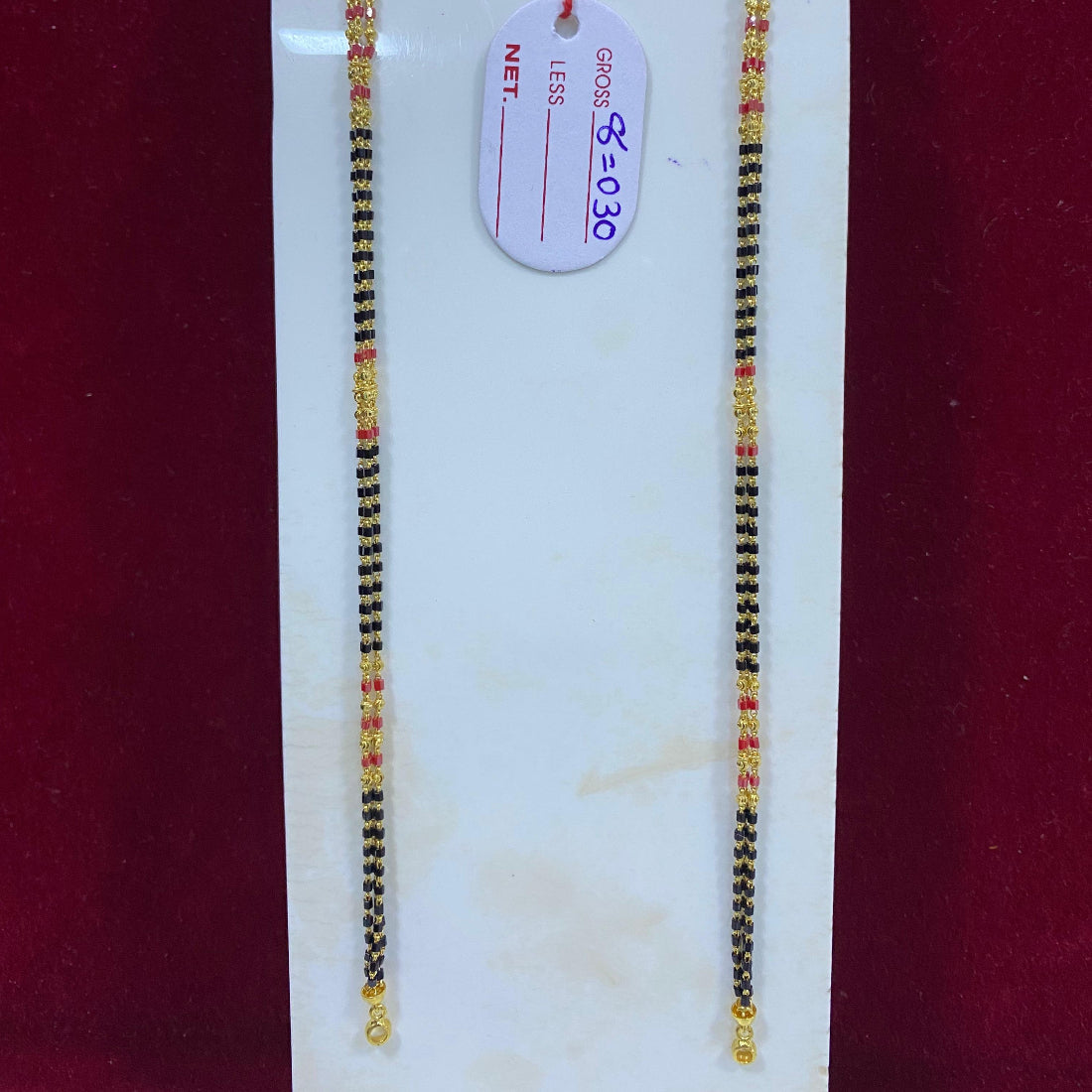 Two black and gold beaded bracelets on a white card with a price tag against a red background.