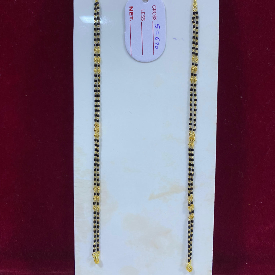 Two gold necklaces on a white card with a red background