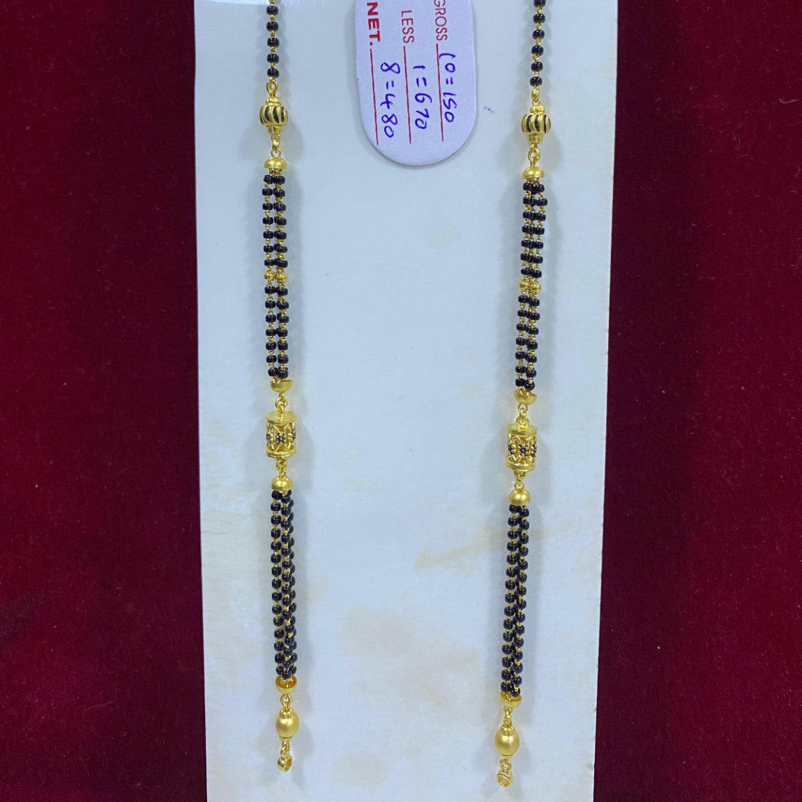 Two black beaded necklaces with gold accents on a white card against a red background.