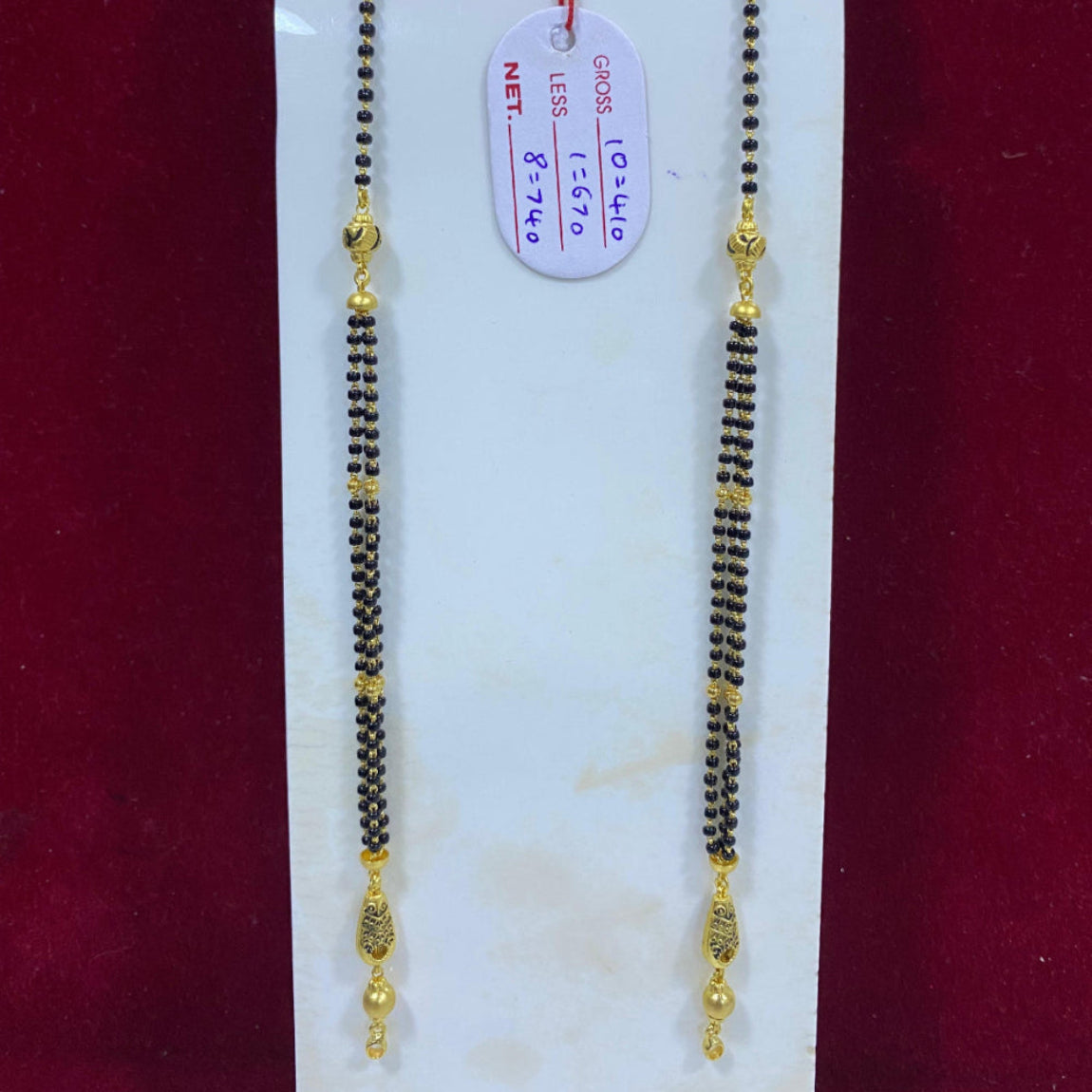 Two gold and black beaded necklaces on a white card with a red background