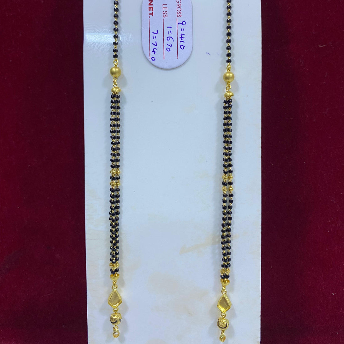 Two gold and black beaded necklaces on a white card with a red background