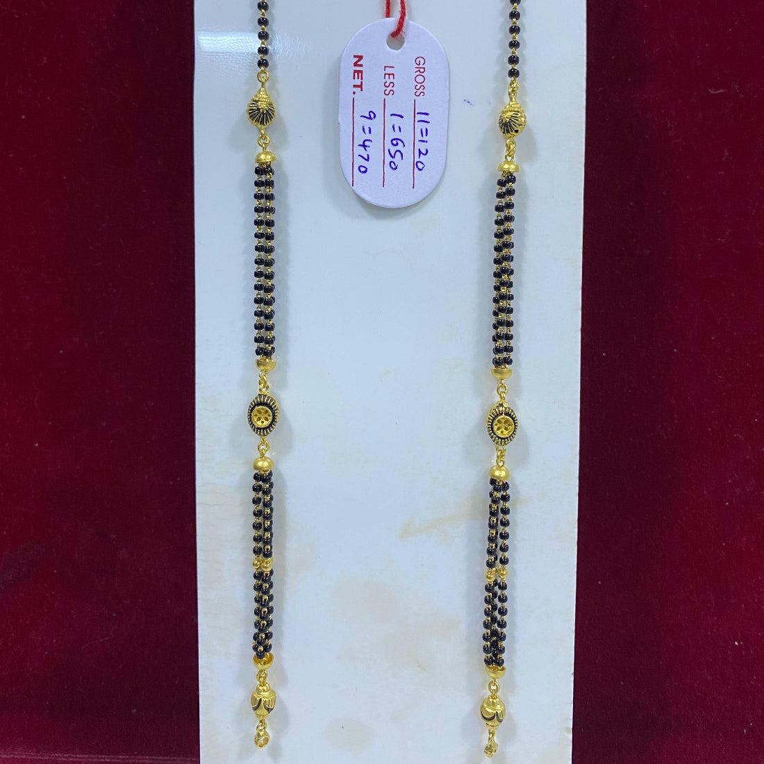 Two gold and black beaded necklaces on a white card with a red background