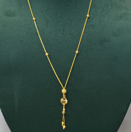 A gold necklace with a delicate chain, small bead accents, and a dangling heart-shaped pendant, displayed on a dark green jewelry bust.