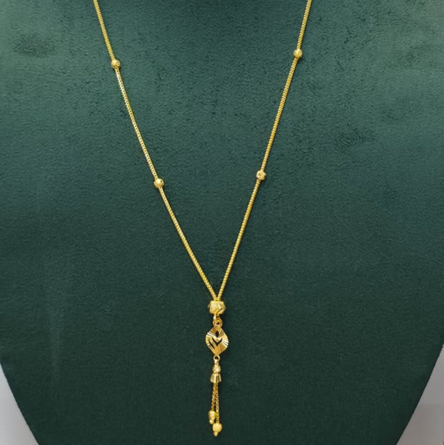 A gold necklace with a delicate chain, small bead accents, and a dangling heart-shaped pendant, displayed on a dark green jewelry bust.
