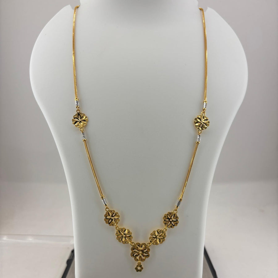 A gold necklace displayed on a white mannequin bust, with a digital scale visible underneath. The necklace features a delicate chain with ornate circular floral motifs and a central pendant.