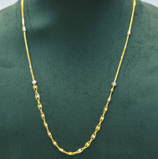 A gold chain necklace with small white bead accents, displayed on a dark green velvet jewelry bust.