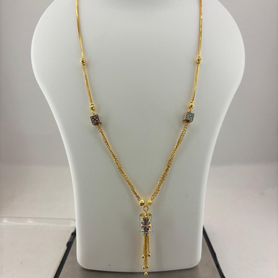 A gold necklace with a tassel pendant and small colorful stone accents, displayed on a white jewelry bust scale on top of a digital scale showing 9.92 grams.