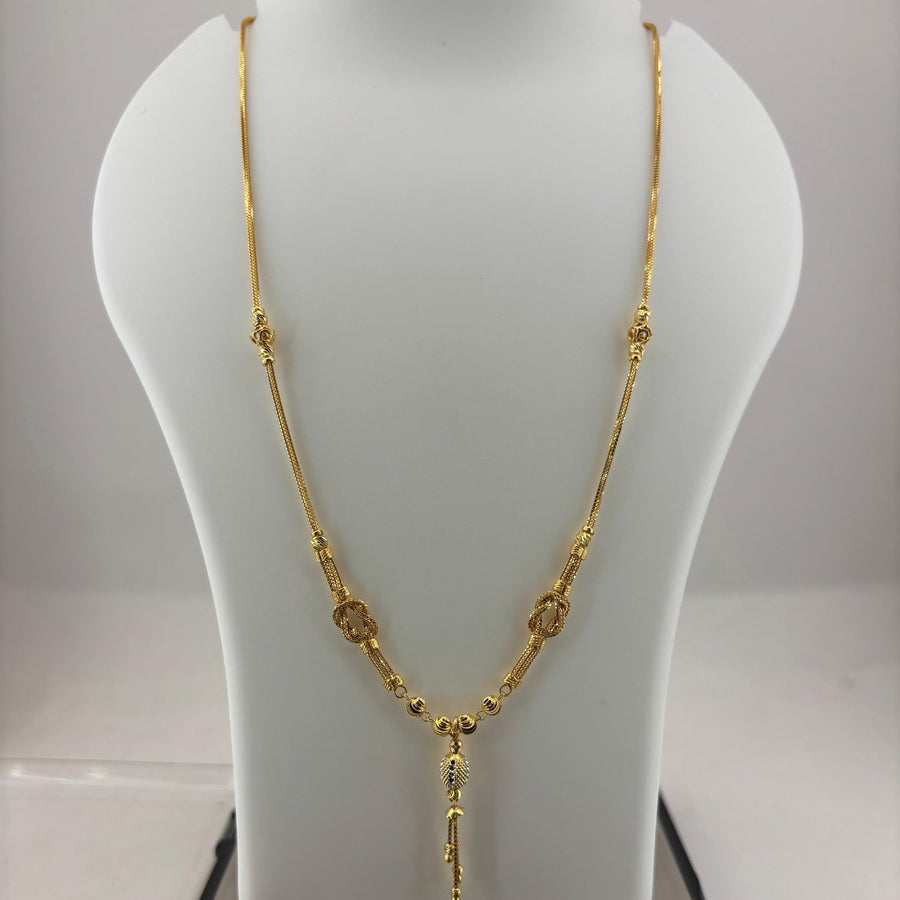 A gold necklace displayed on a white jewelry bust, with a digital scale visible underneath. The necklace features a textured chain with small circular and oval links and a dangling pendant.
