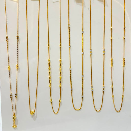 Six gold necklaces with bead details are displayed on a white jewelry stand, each hanging from a hook with a small handwritten price tag attached.